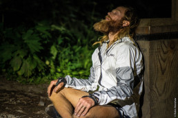 Ultraläufer Timothy Olson sitzend, mit langer Jacke, beim Ausruhen