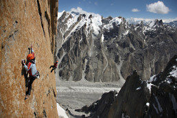Bergsteiger Alexander Huber in vertikaler Felswand vor weitem Panorama großer Berge